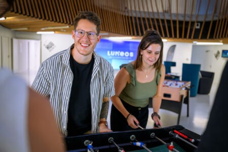 Deux collègues souriants jouent au baby-foot dans les locaux de LUNGOOS.