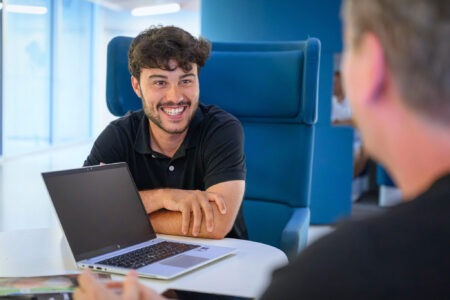 Homme souriant discutant devant un ordinateur portable dans un bureau moderne