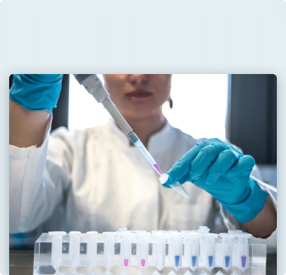 Scientifique en blouse blanche et gants bleus utilisant une pipette pour transférer un liquide violet dans un tube à essai.