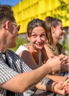 Trois personnes souriantes assises à une table en bois à l'extérieur.